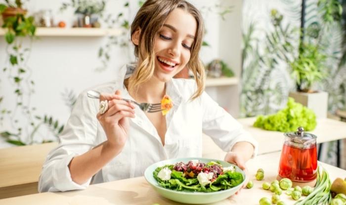 Mujer joven sonriendo y comiendo ensalada.